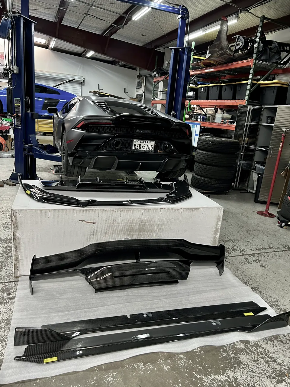 Lamborghini Huracan on a lift in a performance shop with carbon fiber aerodynamic parts laid out for installation.