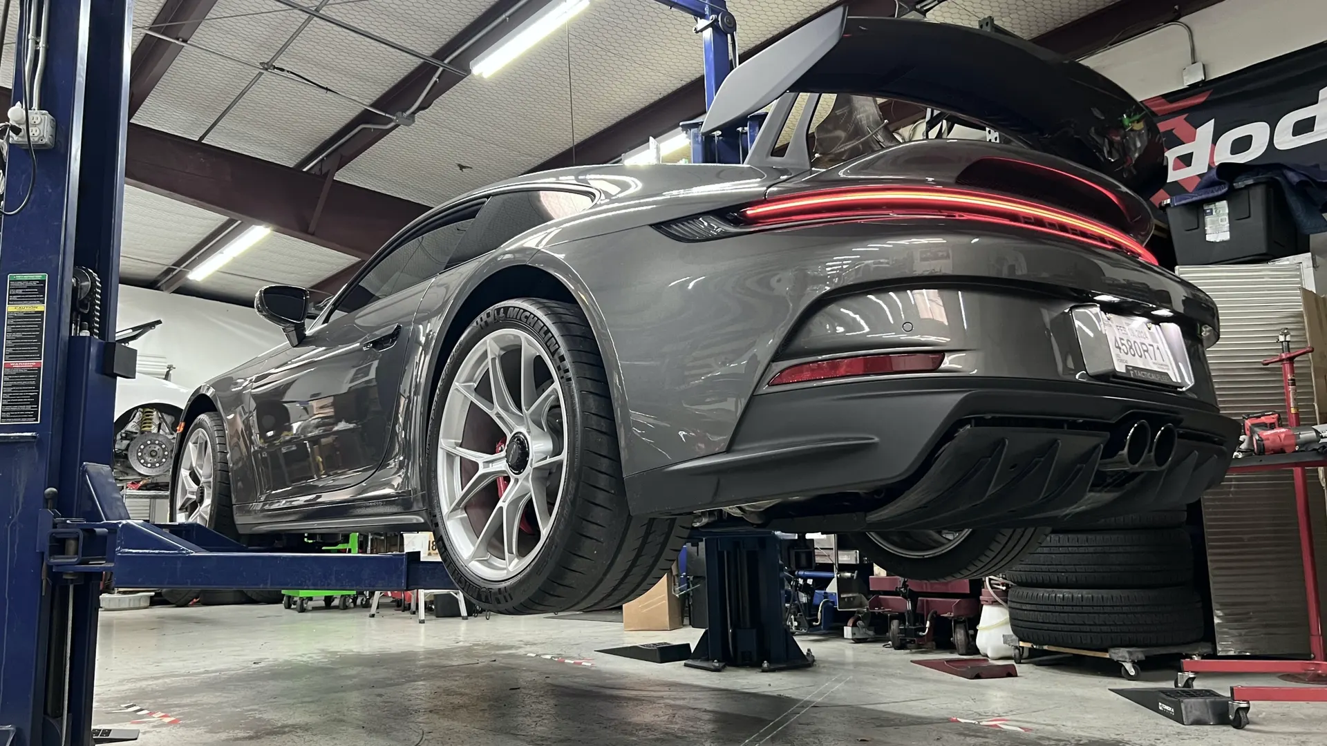 A grey Porsche 911 GT3 on a lift in a performance tuning shop, showcasing its rear diffuser and exhaust.