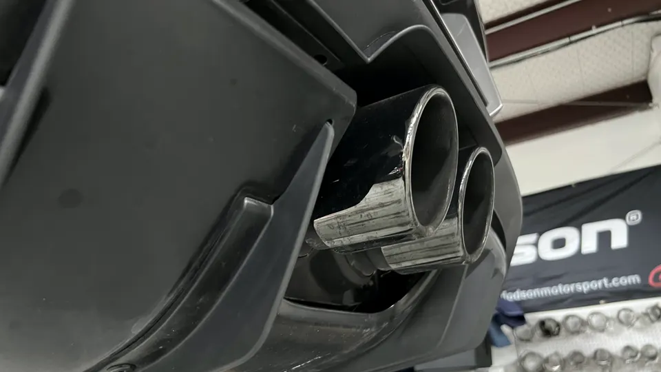 Close-up of a performance exhaust system with dual tips on a car in a shop environment.