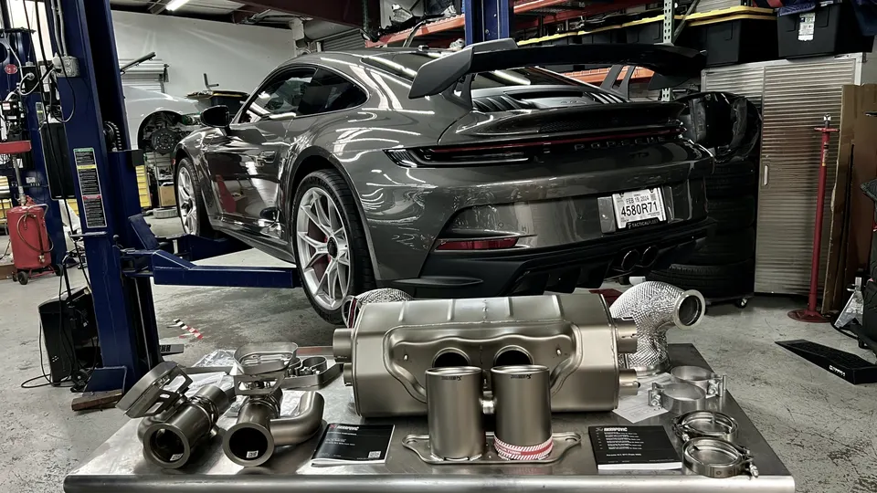 Porsche GT3 on a lift in a shop with an Akrapovic exhaust system laid out for installation.