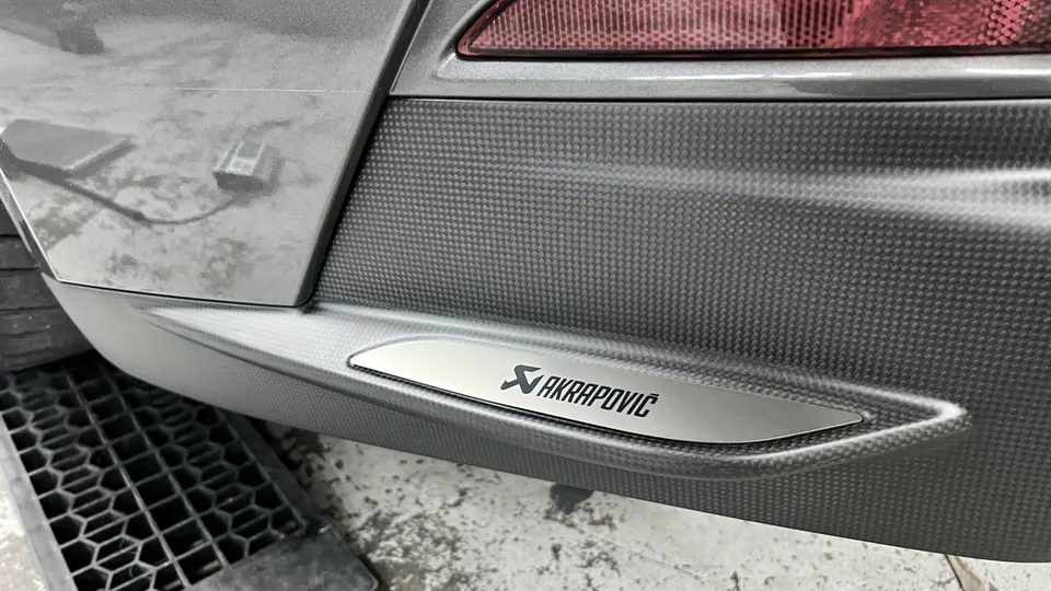 Close-up of an Akrapovic badge on a carbon fiber rear diffuser.