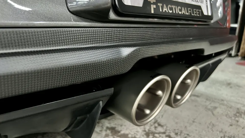 Close-up of a car's rear bumper with carbon fiber trim and dual performance exhaust tips.