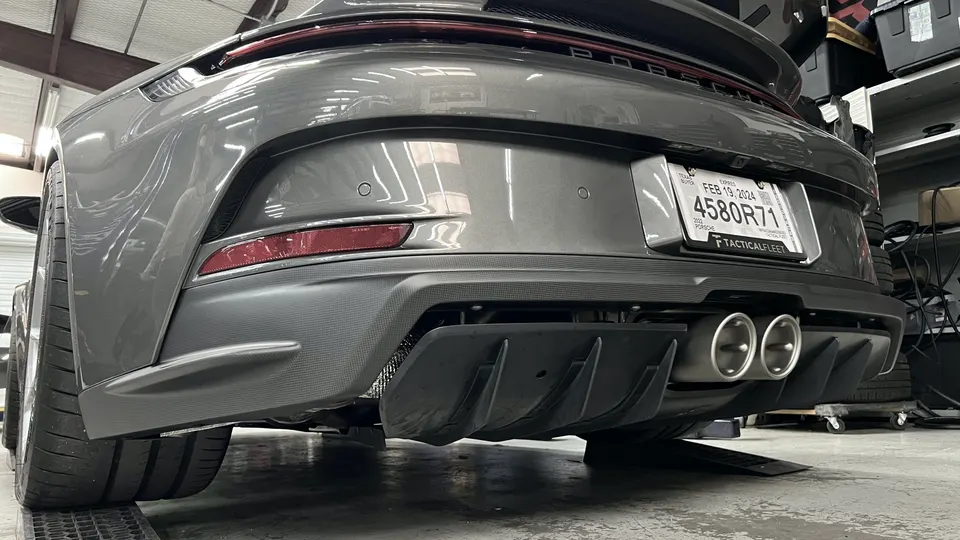 Rear view of a grey Porsche 911 showing the aftermarket rear diffuser and dual exhaust tips in a performance shop.