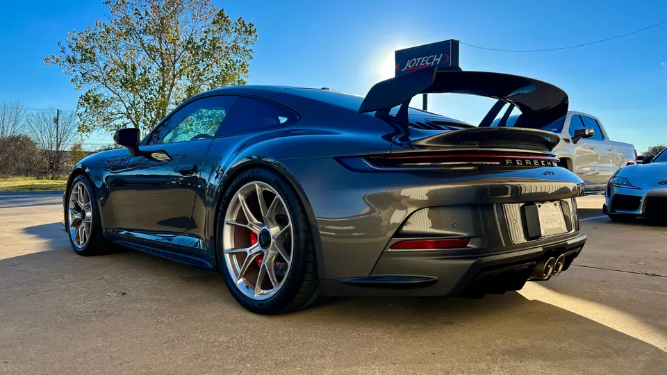 A grey Porsche GT3 with a large rear wing and aftermarket wheels parked outdoors at Jotech Motorsports.