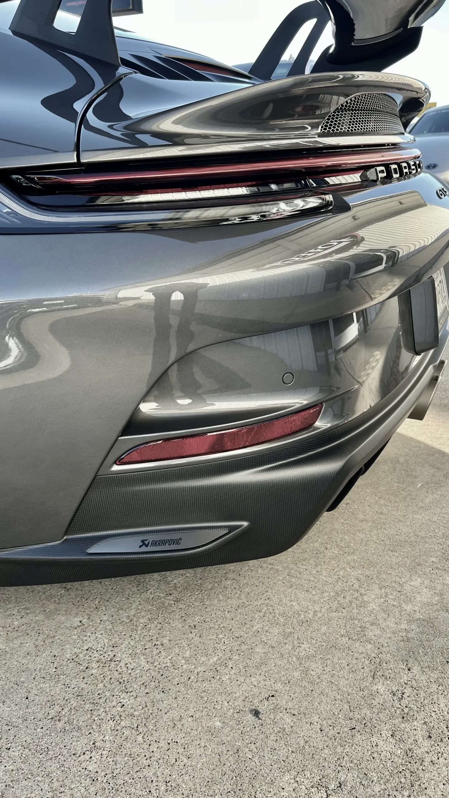 Rear view of a grey Porsche GT3RS showcasing its carbon fiber rear wing, diffuser, and Akrapovic exhaust detail