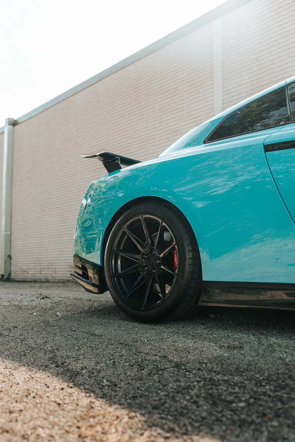Light blue Nissan GT-R with carbon fiber aero, aftermarket black wheels, and red brake calipers parked outdoors.
