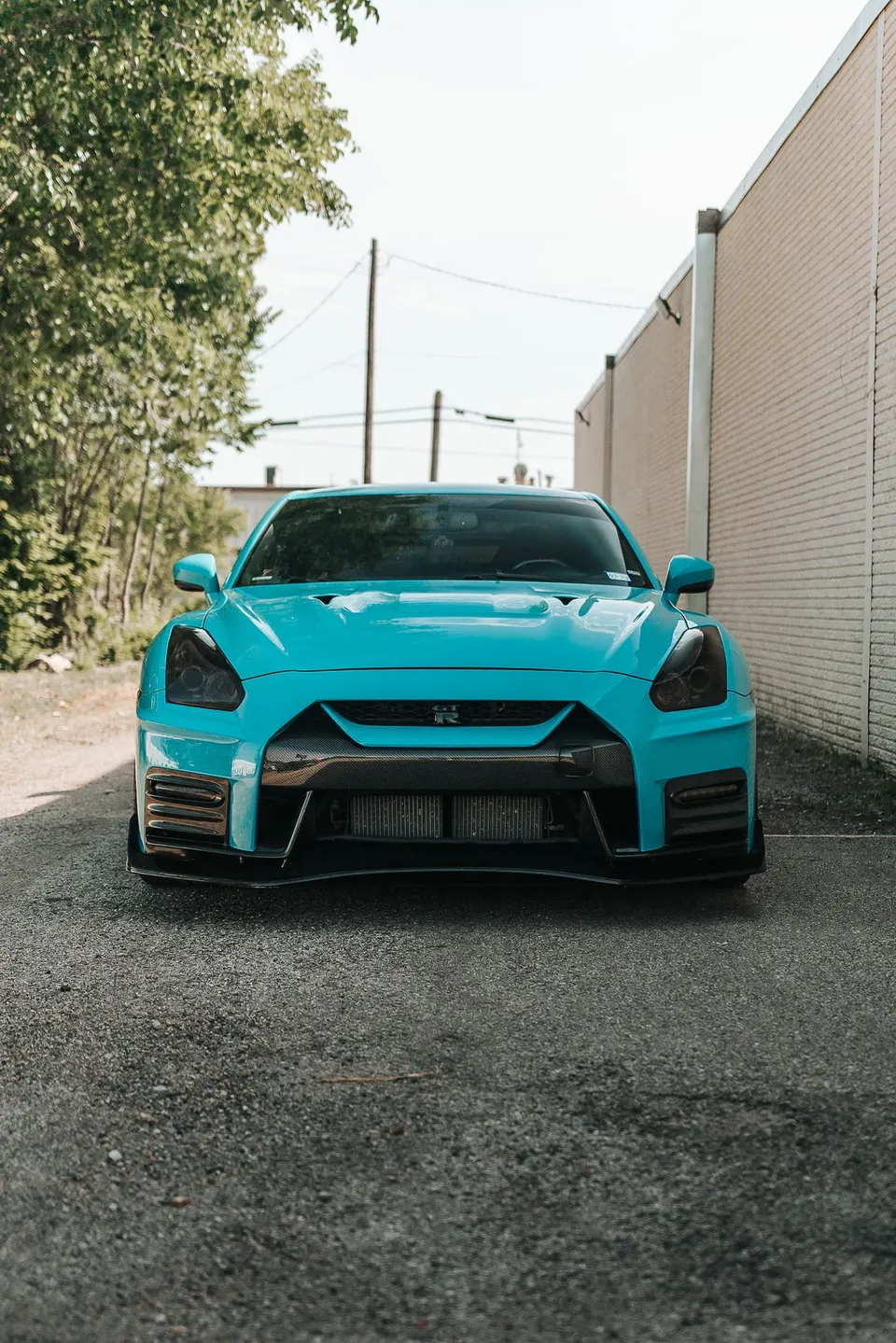 Front view of a custom turquoise Nissan GT-R with a carbon fiber front splitter and modified bumper.