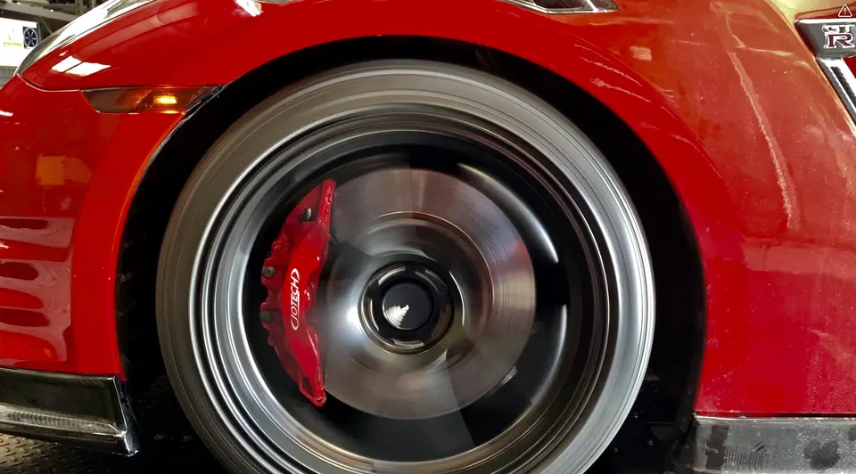 A close-up of a red Nissan GT-R's spinning front wheel with red Jotech brake calipers.
