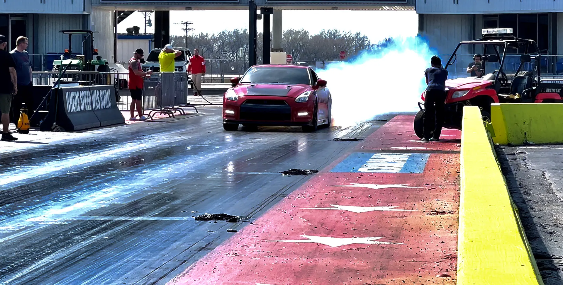 Red Nissan GT-R performing a smoky burnout on a drag strip, preparing for a race.
