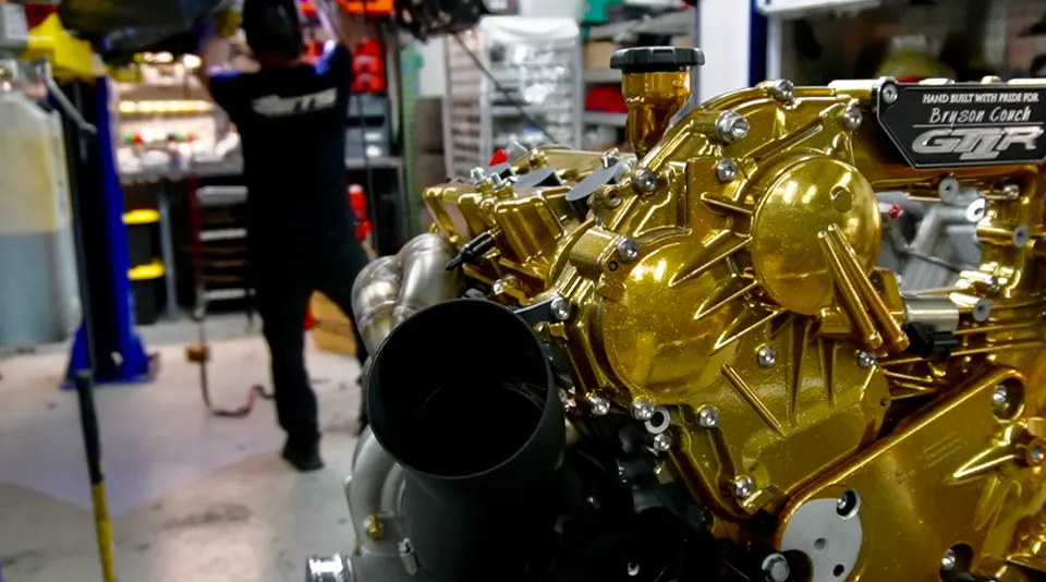 Custom gold-painted VR38DETT engine for a Nissan GT-R being assembled in a performance tuning shop.
