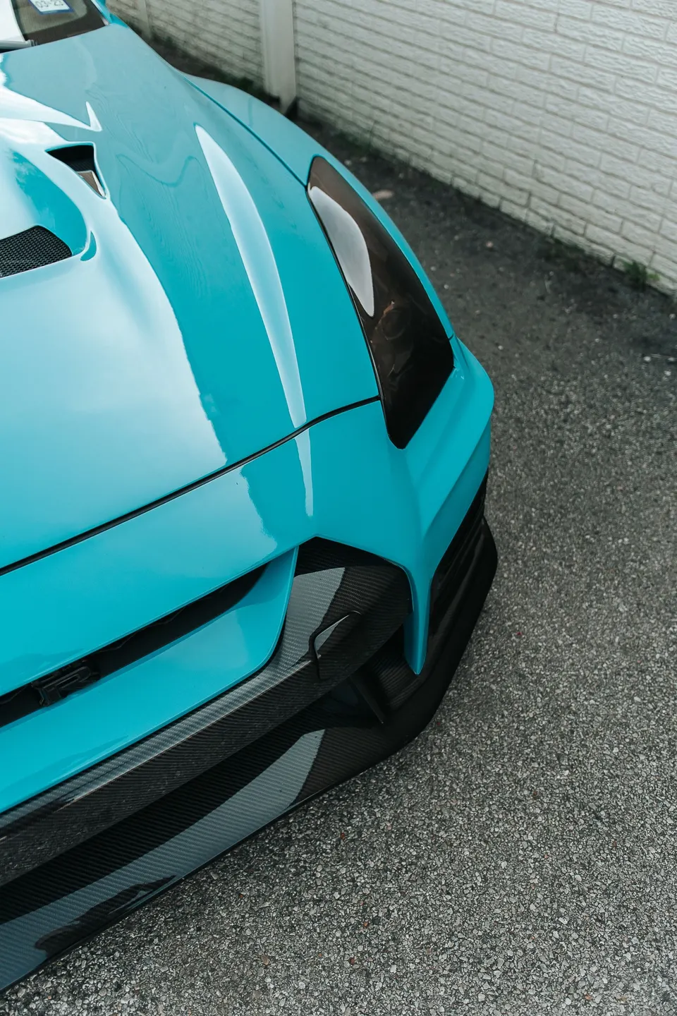 A close-up of the front of a turquoise Nissan GT-R, showcasing its carbon fiber bumper and sleek design.