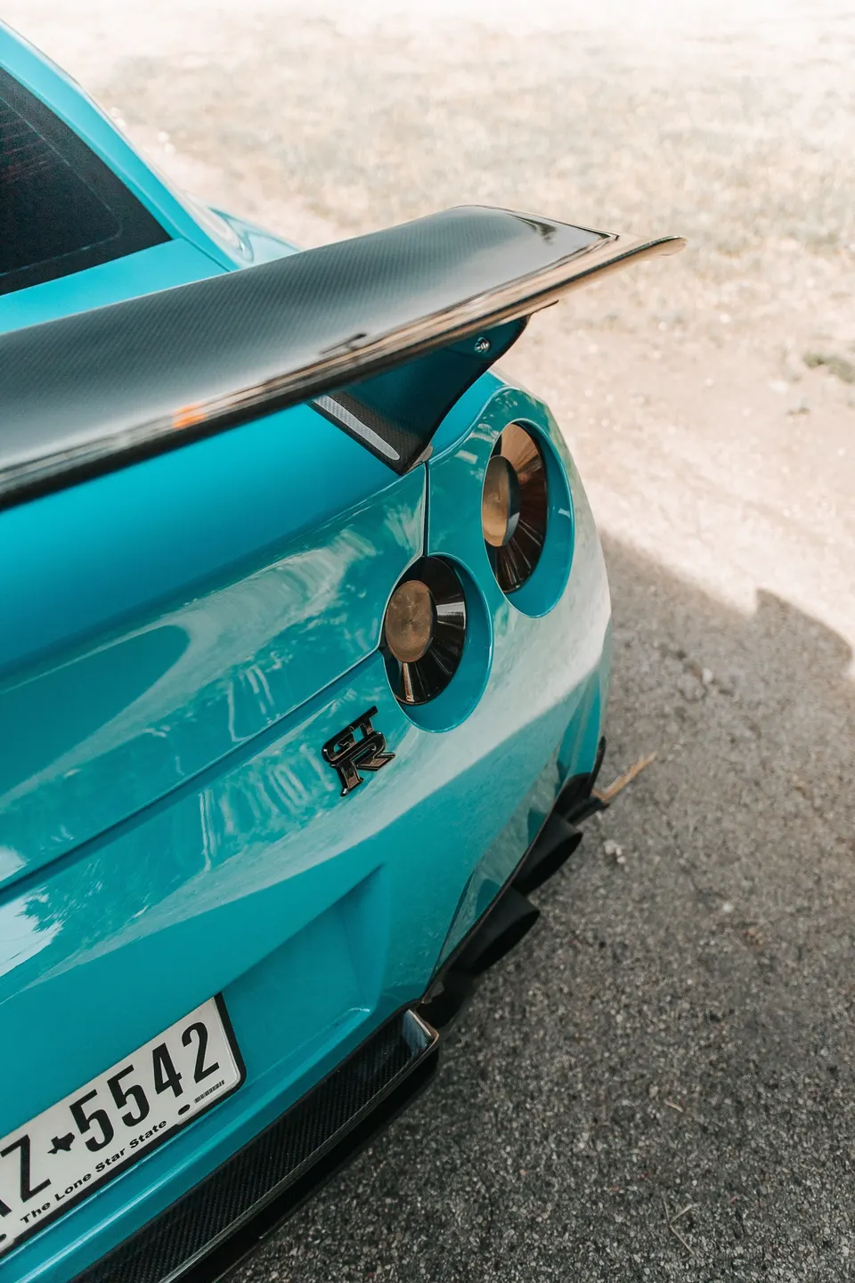 Rear view of a blue Nissan GT-R featuring a carbon fiber wing, round taillights, and a rear diffuser.