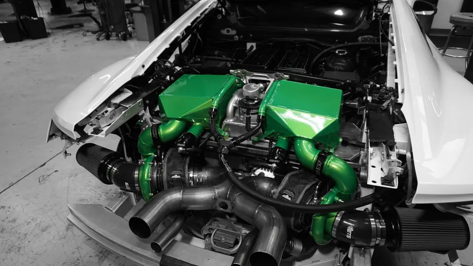 A white car's engine bay showcasing a custom twin-turbo setup with green intake manifolds and polished exhaust piping.