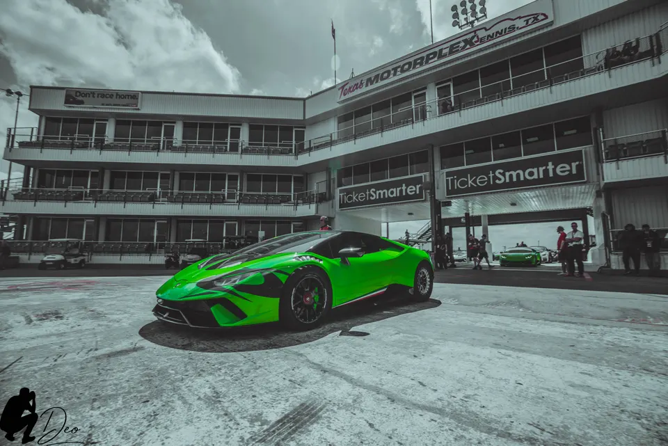 Green Lamborghini Huracan parked at Texas Motorplex drag strip with grandstands in the background.