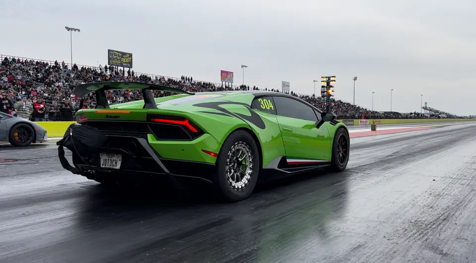 A vibrant green Lamborghini Huracan with a large rear wing and drag wheels on a drag strip, with spectators in the background.