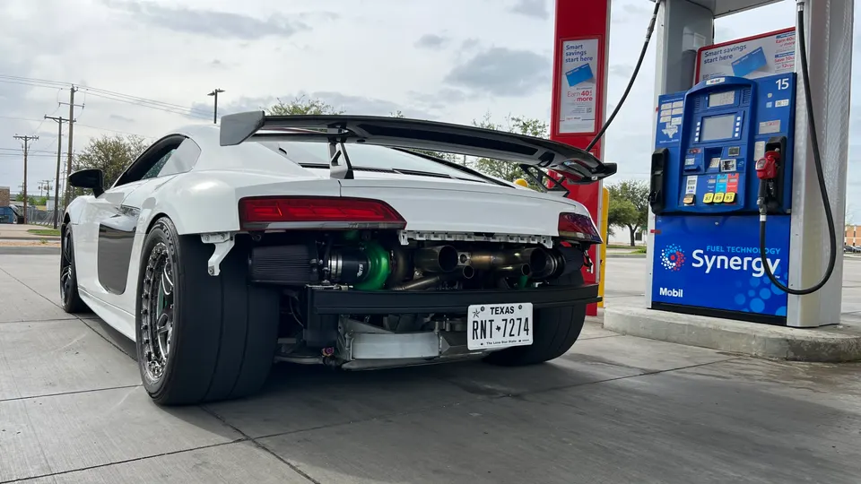 A white Audi R8 with a large exposed turbocharger and custom exhaust system at a Texas gas station.