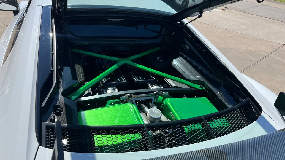 Close-up of a white Audi R8's engine bay with bright green intake manifolds and a green strut bar.