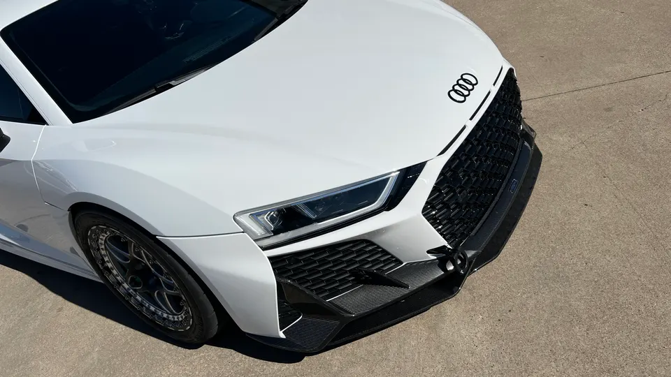 A white Audi R8 with a carbon fiber front splitter and custom wheels parked on concrete.