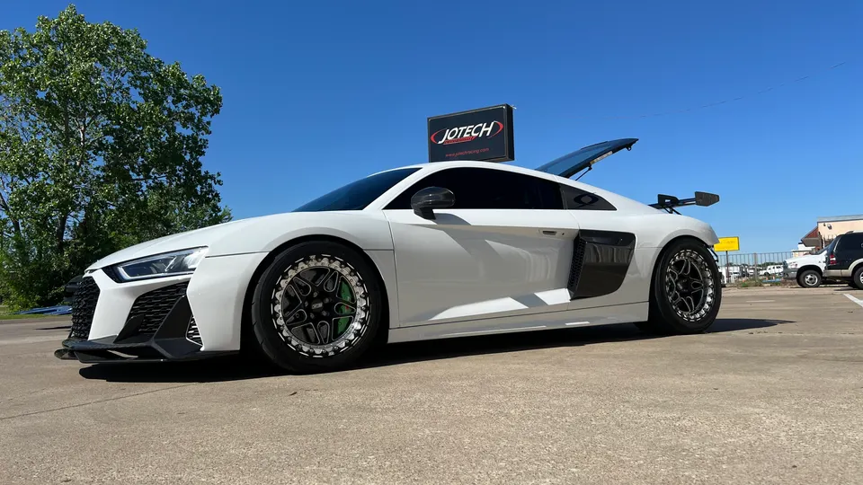 A white Audi R8 with aftermarket BBS wheels, a front splitter, and a rear wing parked outdoors under a Jotech sign.