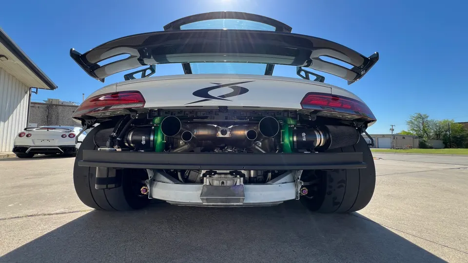 Rear view of a white Porsche 911 with exposed twin turbochargers, custom exhaust, and large rear wing.