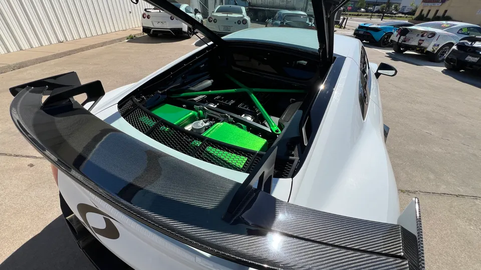 White Lamborghini Huracan with custom green engine bay components and a large carbon fiber rear wing, parked outdoors.