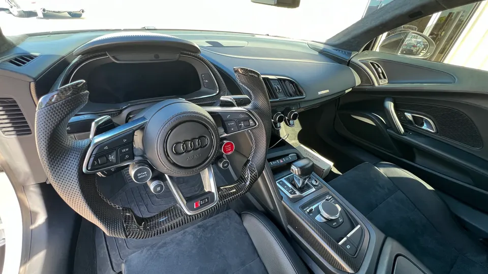 Interior view of an Audi R8, showcasing the carbon fiber steering wheel, digital dashboard, and center console.