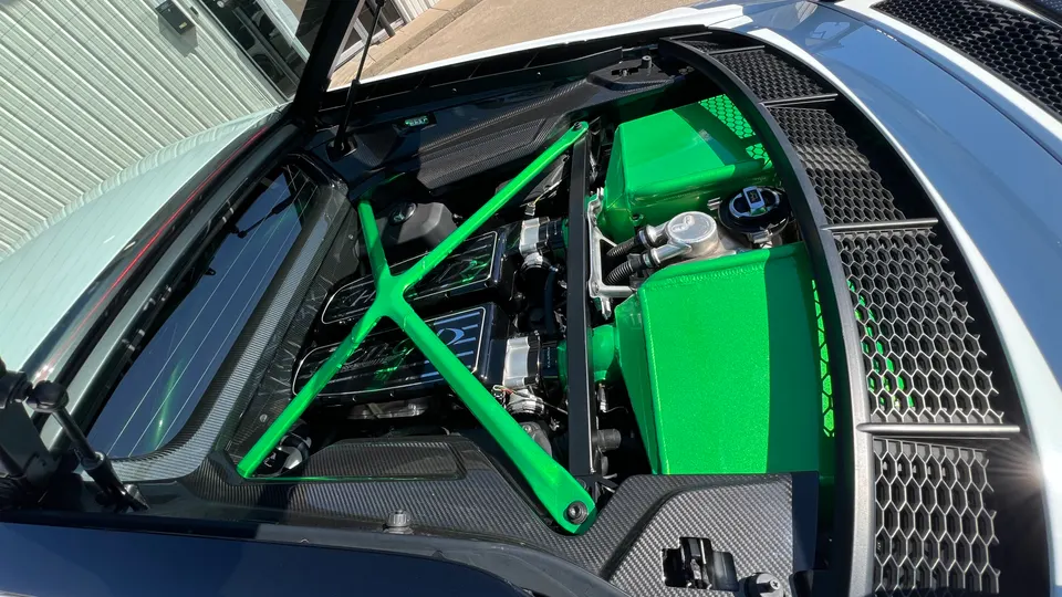 Close-up of a supercar engine bay featuring custom bright green components, a green strut bar, and carbon fiber accents.