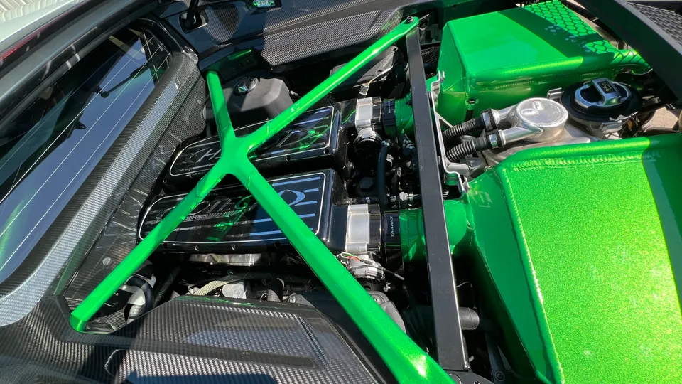 A detailed view of a custom engine bay featuring bright green intake components, a strut bar, and carbon fiber trim.