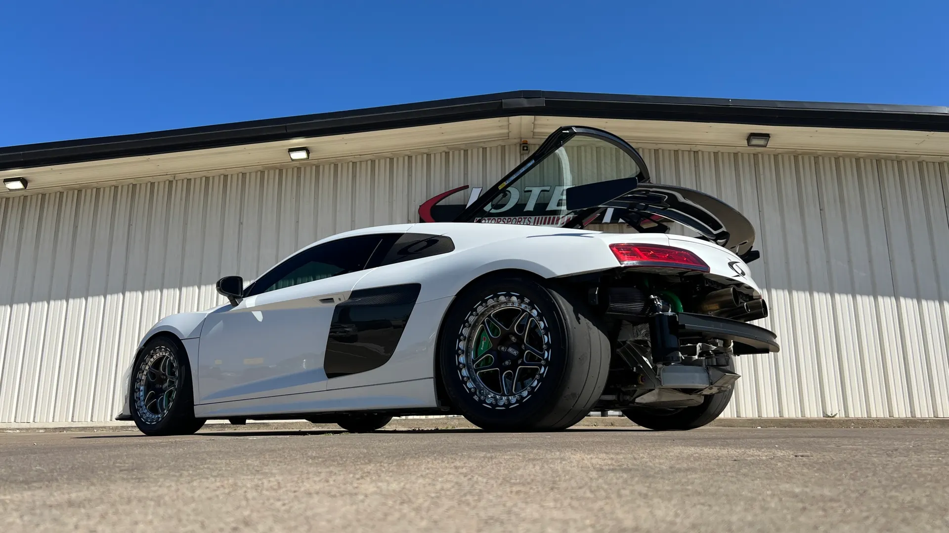 White Audi R8 drag car with exposed rear bumper showing custom exhaust and large drag slicks outside Jotech Motorsports.
