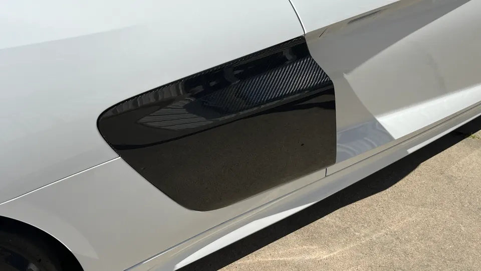 A close-up detail of a white car's side with a carbon fiber fender vent.