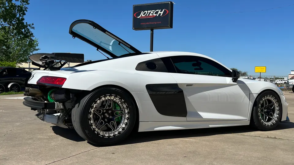 White Audi R8 with exposed turbocharger and drag wheels parked outside Jotech Motorsports performance shop.