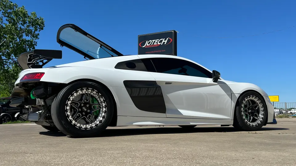 White Audi R8 drag car with exposed engine, large rear wing, and drag wheels parked outside Jotech Motorsports.
