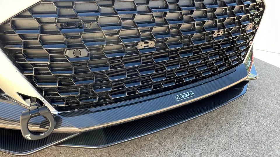 A close-up of a white Hyundai N car's front grille, carbon fiber splitter, and black tow hook with Jotech logo.