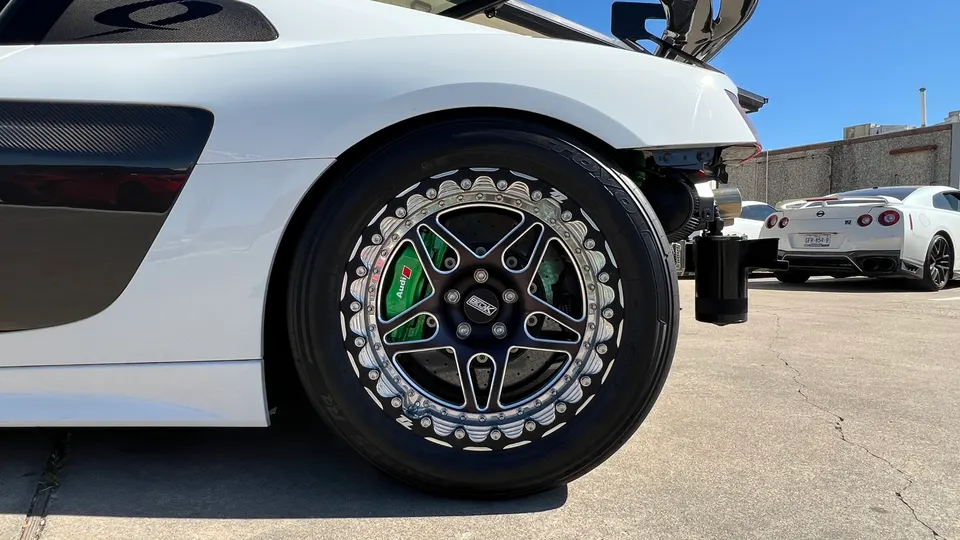 Close-up of a white Audi R8's custom drag wheels with green Audi brake calipers and Toyo tires, with a Nissan GT-R in the background.