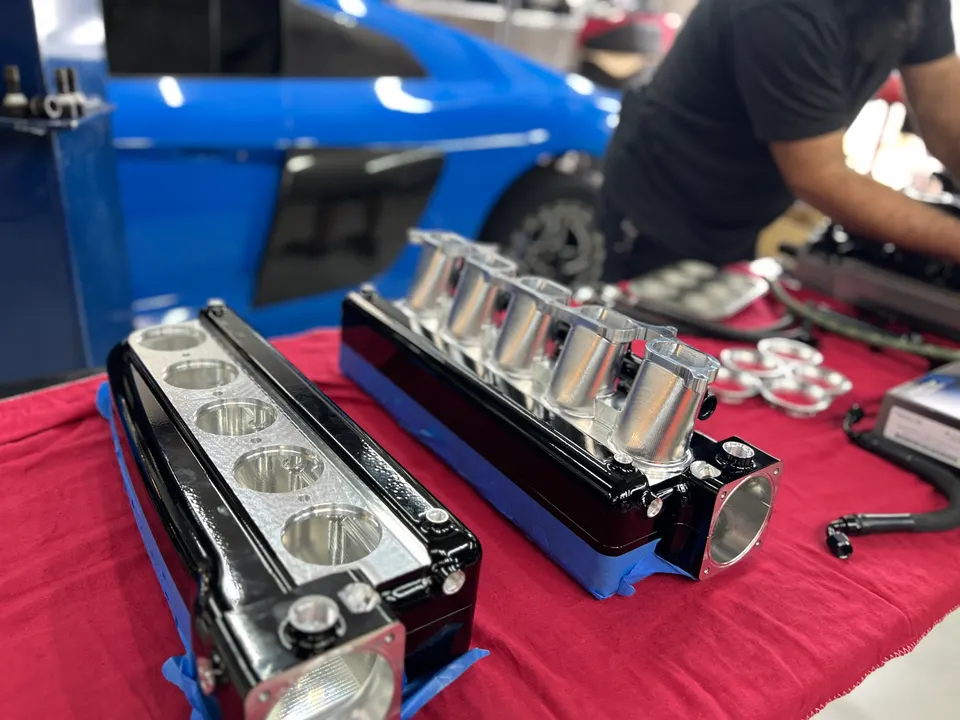 Two black and silver performance intake manifolds with individual throttle bodies on a red table in a tuning shop.