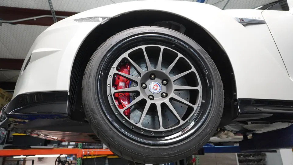 A white Nissan GT-R on a lift showcasing HRE wheels and red brake calipers in a performance shop.