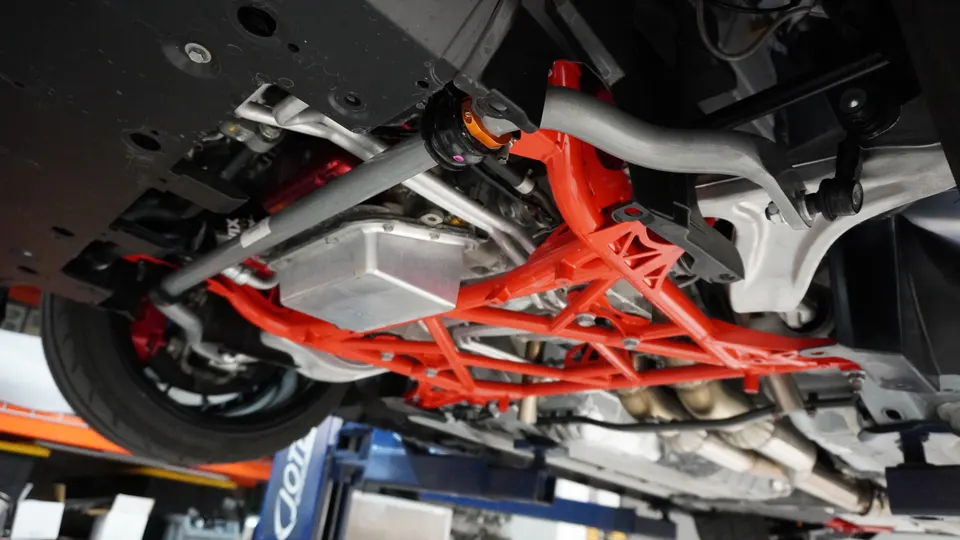 Underside view of a performance car on a lift, showcasing a red subframe, suspension components, and exhaust system.