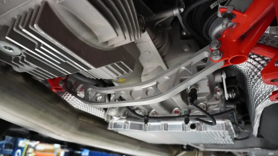 Underside view of a performance car showing the transmission, differential, and a silver chassis brace.