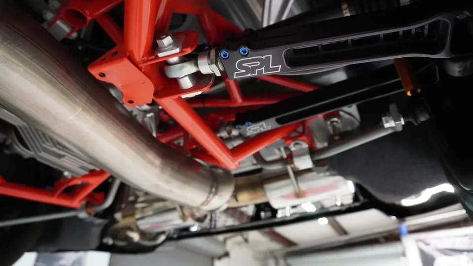 Close-up of a car's undercarriage showing SPL suspension components, red chassis bracing, and a stainless steel exhaust system.