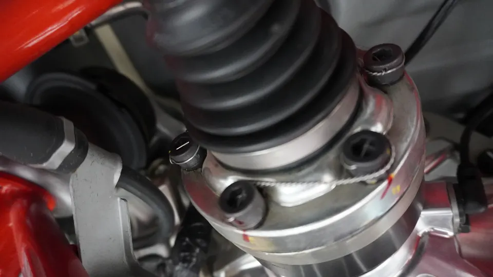 Close-up view of a car's CV boot and axle assembly, secured with safety wire on the bolts.