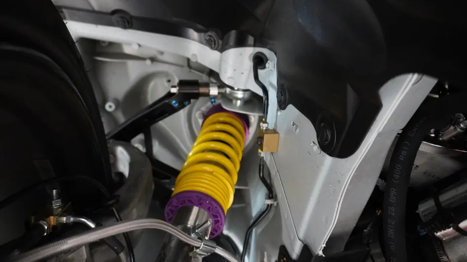 Close-up view of a yellow and purple coilover suspension system installed on a car's chassis.