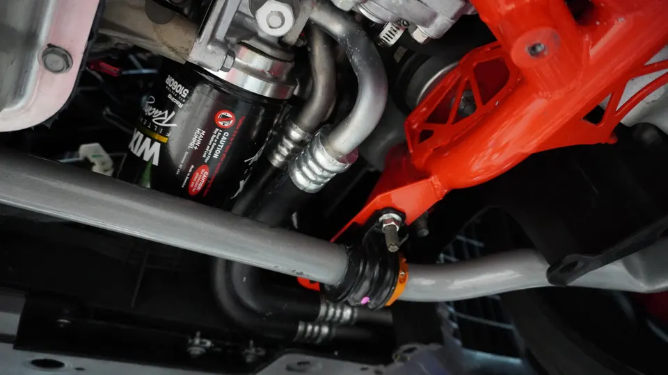 Close-up view of a car's underside showing a Wix Racing oil filter, sway bar, and orange chassis brace.
