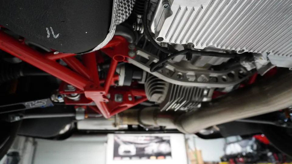 Underside view of a performance car, highlighting custom red suspension components, differential, and exhaust system.