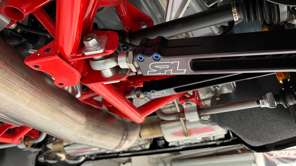 Close-up of a car's undercarriage featuring red subframe, SPL adjustable control arms, and exhaust system.