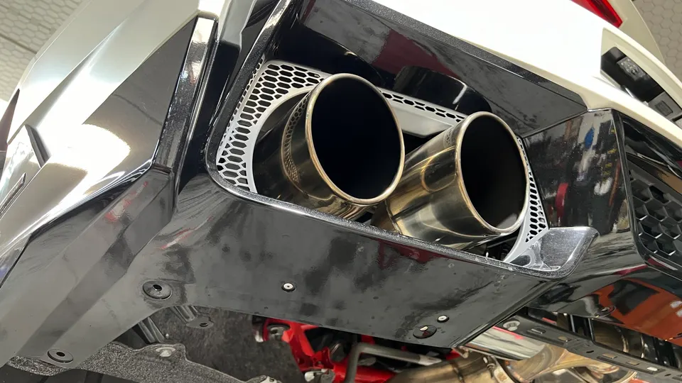 Close-up of a car's rear bumper featuring dual polished exhaust tips integrated into a black honeycomb diffuser.