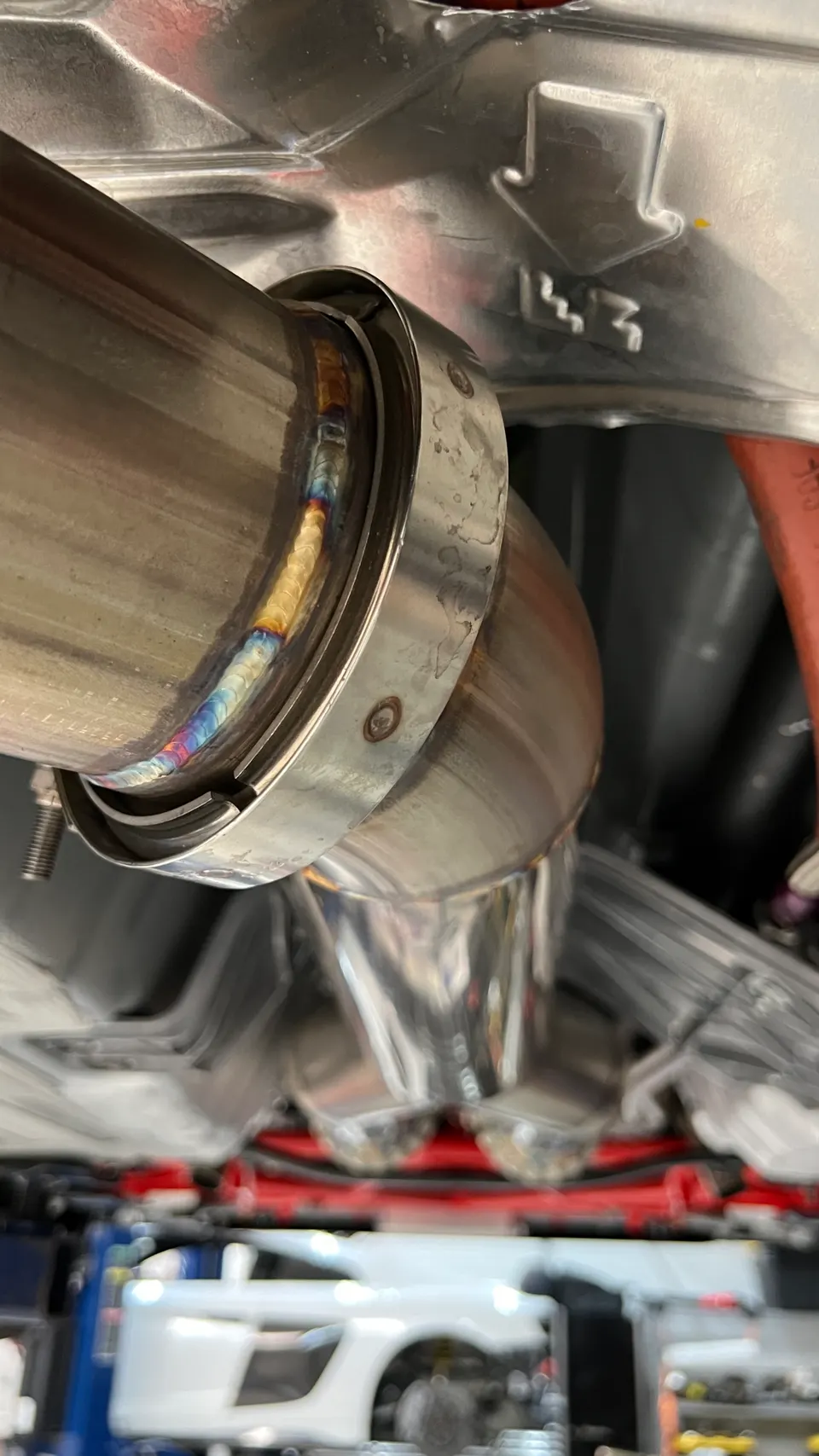 Close-up of a custom stainless steel exhaust system with colorful welds, installed on a performance car in a shop.