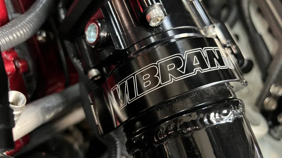 A close-up of a black Vibrant Performance induction pipe in an engine bay, showcasing the brand logo and welded construction.