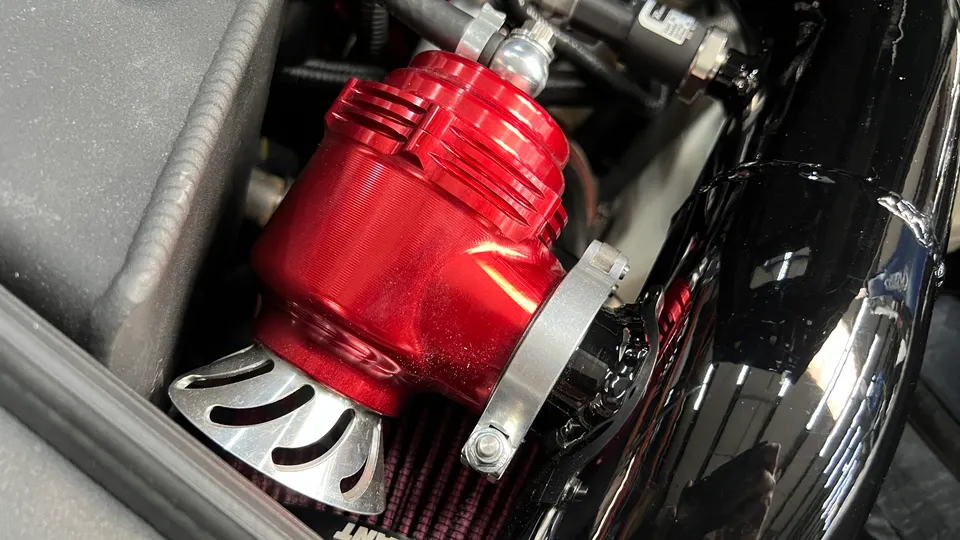A close-up of a red aftermarket blow-off valve installed in an engine bay.