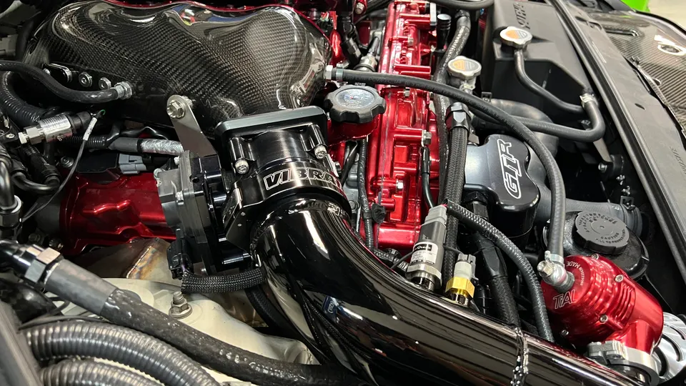 Close-up of a high-performance Nissan GT-R engine bay featuring a carbon fiber intake, Vibrant throttle body, and Tial blow-off valve.