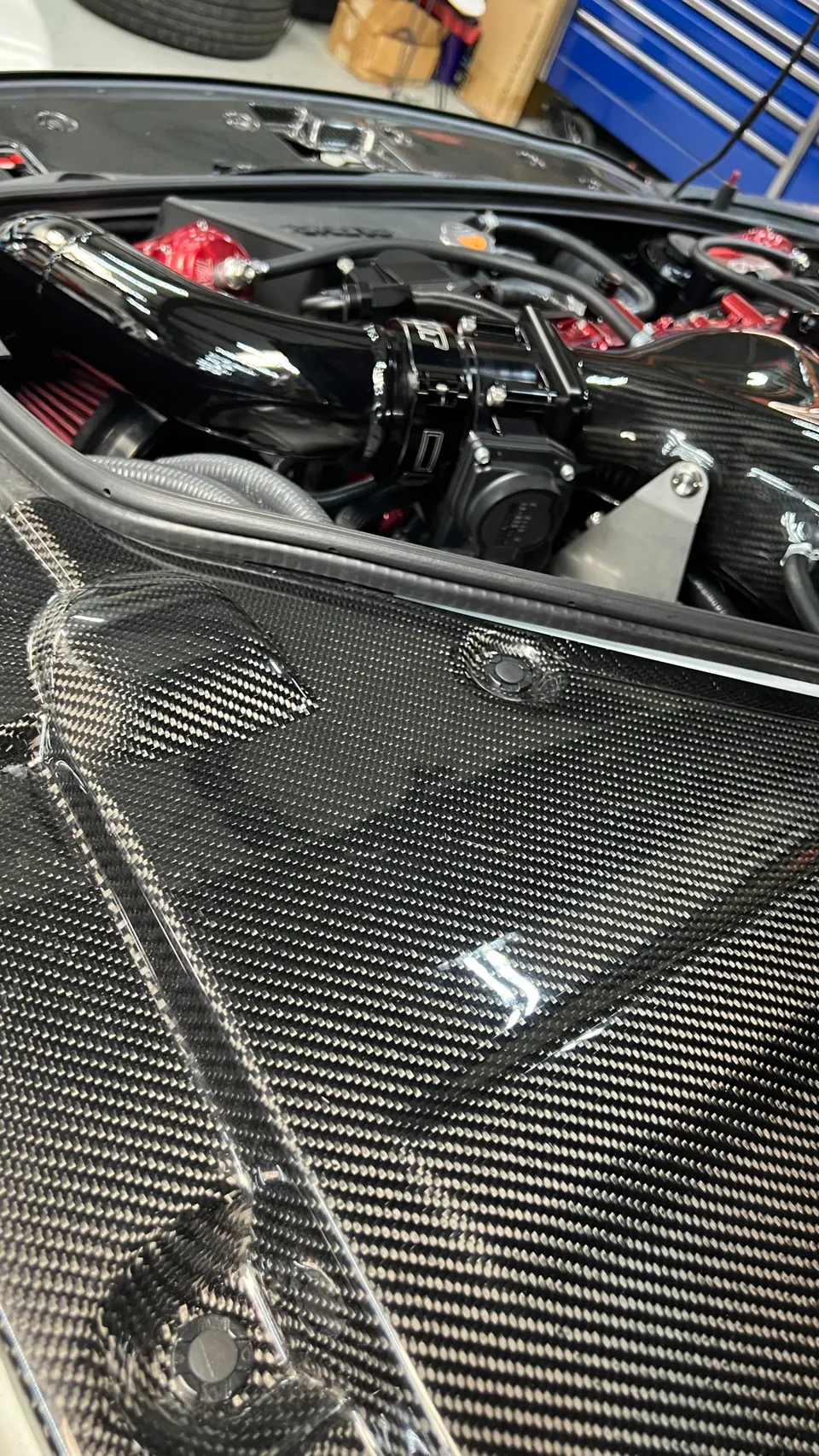 Close-up of a high-performance engine bay featuring a carbon fiber cover, aftermarket intake, and blow-off valve.
